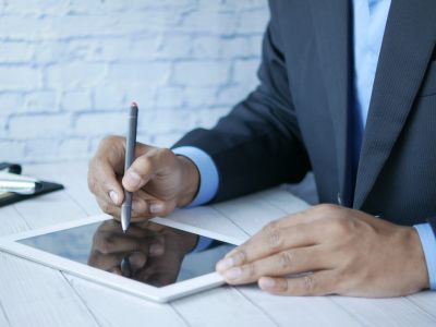 Business Mann in grauem Anzug sitzt an Tisch und zeichnet mit Stift auf Tablet. Management