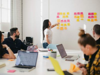 Frau an einem Flipboard mit Zetteln und Männer und Frauen um einen Konferenztisch. Business Development.